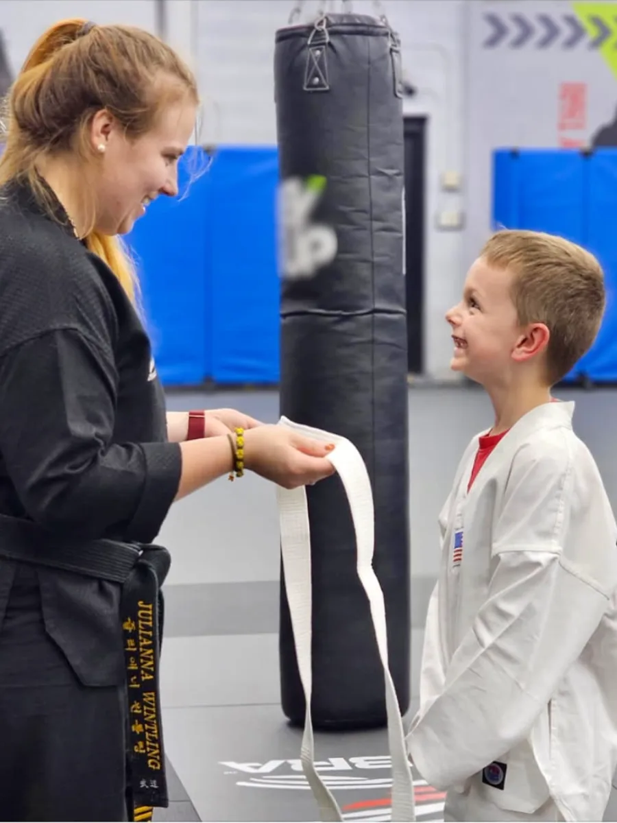 Instructor tying a new white belt on a young martial arts student at Rise Up NJ in Atco